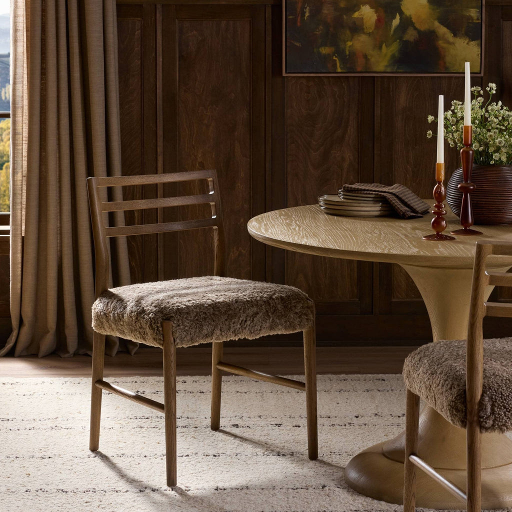 Dining room with wooden chairs and a round table, featuring a floral painting on the wall.