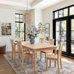 Dining room with wooden table and chairs, floral arrangement, and large windows.
