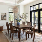 Dining room with wooden table and chairs, vase of flowers, and large windows.