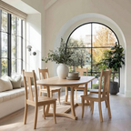 Dining area with wooden table and chairs in a bright room with large windows.