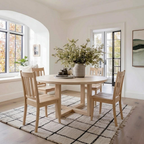 Dining room with wooden table and chairs on a checkered rug, large windows, and a vase of flowers.