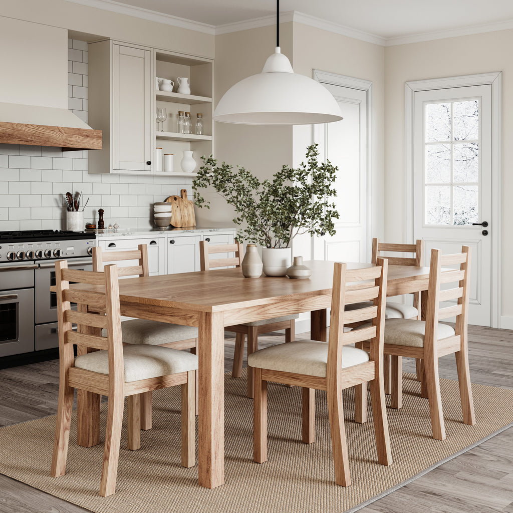 Oak dining table with matching chairs in a bright, well lit dining room with white cabinets and wall tiles.