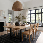 Dining room with wooden table and chairs, large windows, and a wicker pendant light.