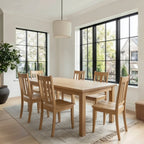 Wooden dining table with chairs in a bright room with large windows.