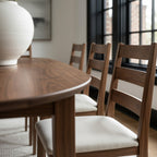 Dining room with wooden table and chairs, large windows, and a white rug.