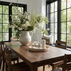 Dining room with a wooden table, chairs, and a large vase of white flowers.