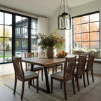 Dining room with wooden table and chairs, large windows, and a vase of flowers.