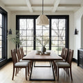 Dining room with wooden table and chairs in a well-lit room with large windows.