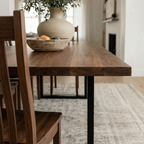 Wooden dining table with a vase and fruit on top, in a home setting.