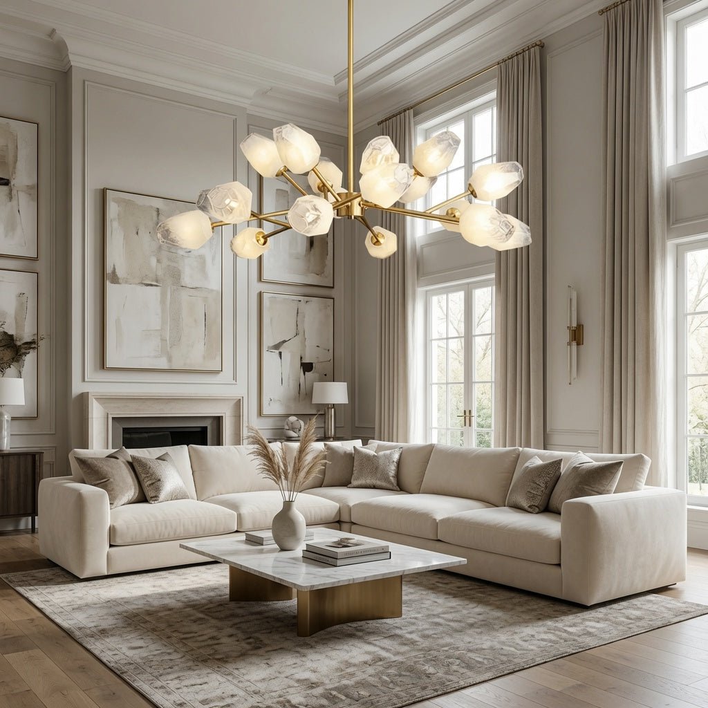 A luxury modern living room featuring a large multi-light crystal chandelier with a gold frame, a cream sectional sofa, a marble coffee table, and elegant beige walls with classical molding.